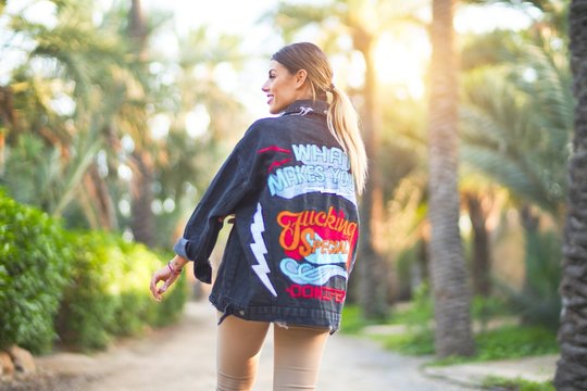 Young beautiful woman wearing denim jacket standing backwards at the town park