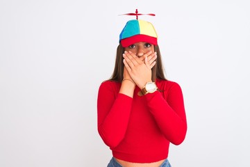 Young beautiful girl wearing fanny cap with propeller standing over isolated white background shocked covering mouth with hands for mistake. Secret concept.