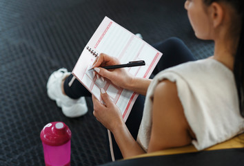 Young woman making her workout schedule in notebook indoors, above view
