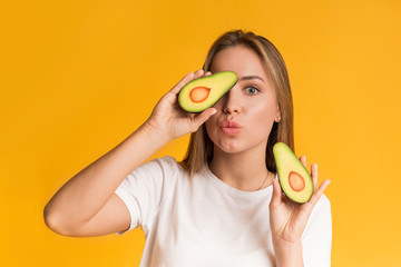 Cheerful Girl Posing With Avocado Halves On Yellow Background In Studio