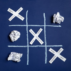 Conceptual photo. The torment of creativity. Tic-tac-toe game. Crumpled sheets of paper on a blue background and paper crosses. Flat lay, top view.