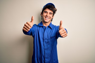 Young mechanic man wearing blue cap and uniform standing over isolated white background approving...