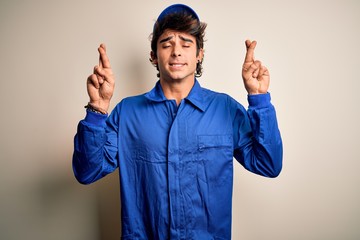 Young mechanic man wearing blue cap and uniform standing over isolated white background gesturing...