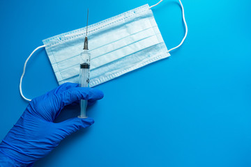 Fototapeta na wymiar Hand in a medical glove holding a syringe with a vaccine medical mask on a blue background. The vaccine for coronavirus concept