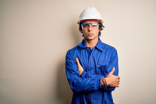 Young constructor man wearing uniform and security helmet over isolated white background skeptic and nervous, disapproving expression on face with crossed arms. Negative person.
