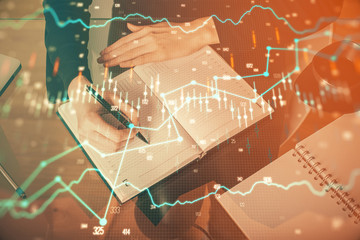 Forex chart hologram on hand taking notes background. Concept of analysis. Multi exposure