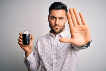 Young handsome man drinking a cup of hot coffee over white isolated background with open hand doing stop sign with serious and confident expression, defense gesture