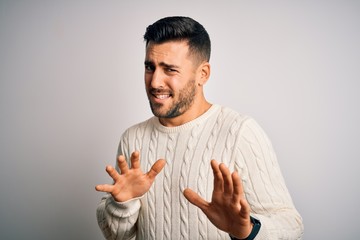 Young handsome man wearing casual sweater standing over isolated white background disgusted...