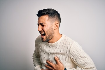 Young handsome man wearing casual sweater standing over isolated white background with hand on stomach because nausea, painful disease feeling unwell. Ache concept.