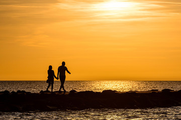 silhouette of couple walking on the pier during the golden hour of sunset