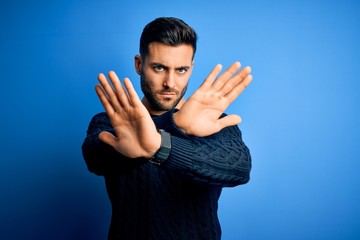 Young handsome man wearing casual sweater standing over isolated blue background Rejection...