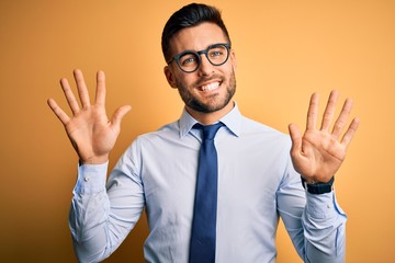 Young handsome businessman wearing tie and glasses standing over yellow background showing and pointing up with fingers number ten while smiling confident and happy.