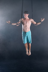 Circus artist on the aerial straps with Strong muscles on black background wearing casual clothes 
