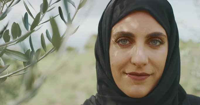 Portrait of a beautiful muslim woman wearing a black hijab headscarf outdoors with green foliage olive trees, mysterious woman in nature
