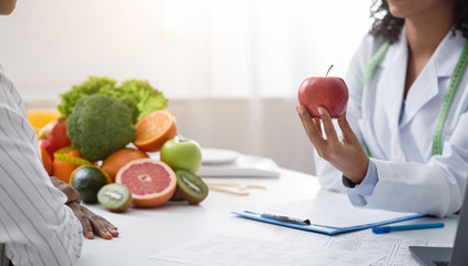 Cropped of nutritionist holding red apple in front of patient