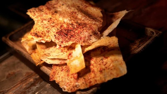 Thin baked bread snacks with spices on a wooden cutting board under warm muffled light, close-up. Bread slices with tomato paste, red pepper and herbs.