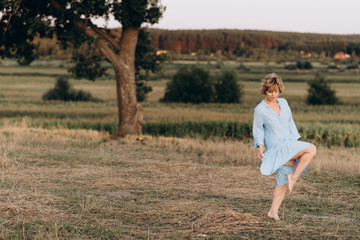 Beautiful free woman in a light dress dances in the summer in a field near a large tree. Soft selective focus.