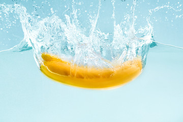 Yummy banana splashing into clear water against blue background