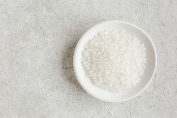 Salt in a bowl on gray stone table. Sea salt flat lay, top view. Spa skincare concept. Natural/Organic spa cosmetics products