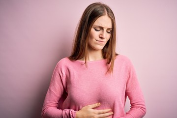 Obraz premium Young beautiful redhead woman wearing casual sweater over isolated pink background with hand on stomach because indigestion, painful illness feeling unwell. Ache concept.