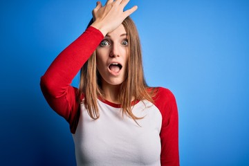 Young beautiful redhead woman wearing casual t-shirt over isolated blue background surprised with...