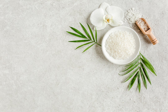 Spa skincare concept. Natural/Organic spa cosmetics products, sea salt and tropic palm leaves on gray marble table from above. Spa background with a space for a text, flat lay, top view.