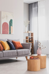 Flowers in pastel pink vase on wooden coffee table in front of grey scandinavian couch with colorful pillows