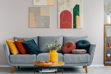 Colorful abstract painting above grey couch with pillows in scandinavian design interior