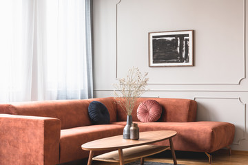 Dry flowers in stylish dark vase on wooden coffee table in front of ginger colored corner sofa
