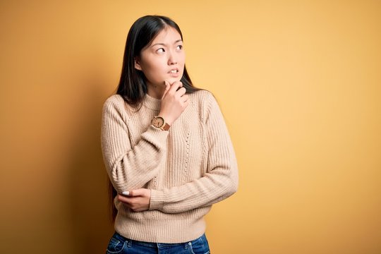 Young beautiful asian woman wearing casual sweater over yellow isolated background Thinking worried about a question, concerned and nervous with hand on chin