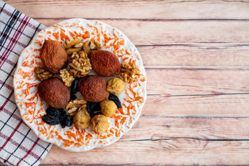 figs, raisins, apricots, nuts in a saucer on a kitchen napkin on a wooden background