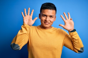 Young handsome latin man wearing yellow casual sweater over isolated blue background showing and...