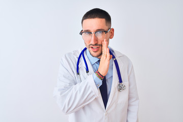 Young doctor man wearing stethoscope over isolated background hand on mouth telling secret rumor, whispering malicious talk conversation