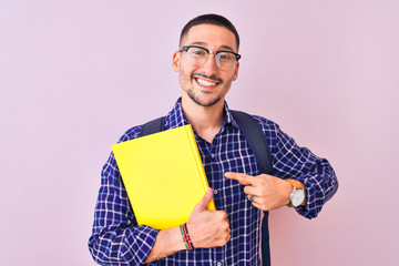 Young handsome student man holding a book over isolated background very happy pointing with hand and finger