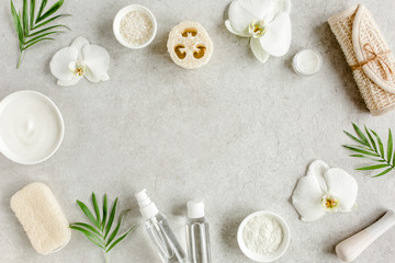 Obraz na płótnie Canvas Spa treatment concept. Natural/Organic spa cosmetics products, sea salt, massage brush, tropic palm leaves on gray marble table from above. Spa background with a space for a text, flat lay, top view