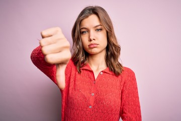 Young beautiful blonde casual girl over pink isolated background looking unhappy and angry showing rejection and negative with thumbs down gesture. Bad expression.