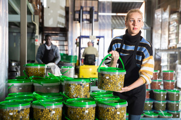 Female worker stocks plastic containers and cans with olives in warehouse