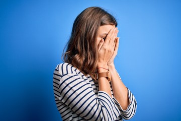 Young beautiful blonde girl wearing casual sweater standing over blue isolated background with sad expression covering face with hands while crying. Depression concept.