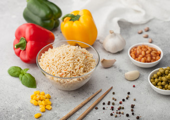Glass bowl with boiled long grain basmati rice with vegetables on light table background with sticks and paprika pepper with corn, beans and peas with garlic and basil.
