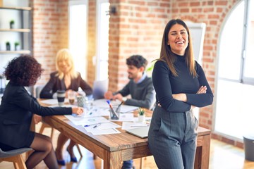 Group of business workers working together. Young beautiful woman standing smiling happy looking at the camera at the office