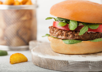Healthy vegetarian meat free burger on round chopping board with vegetables on light table background with potato wedges.