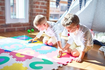 Adorable blonde twins playing with cars around lots of toys at kindergarte