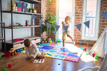 Adorable blonde twins playing around lots of toys at kindergarten