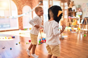 Adorable blonde twins playing wearing monkey mask around lots of toys at kindergarten