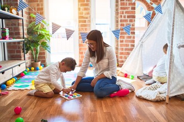 Beautiful teacher and toddler learning maths using numbers puzzle game around lots of toys at kindergarten