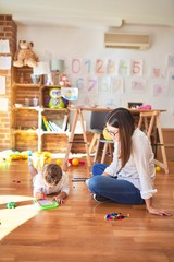 Beautiful teacher and toddler drawing using digital board around lots of toys at kindergarten