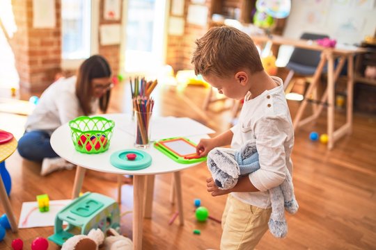 Beautiful teacher and toddler drawing using digital board around lots of toys at kindergarten