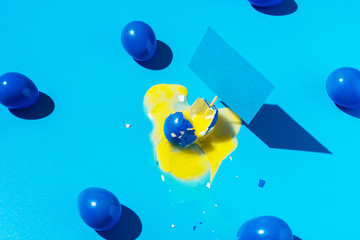 Blue background with Easter eggs, a broken egg with a leaking yolk, minimalism, hard shadows