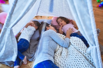 Young beautiful teacher and toddlers lying down over blanket inside tipi at kindergarten