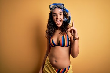 Young beautiful woman with curly hair on vacation wearing bikini and diving googles pointing finger...